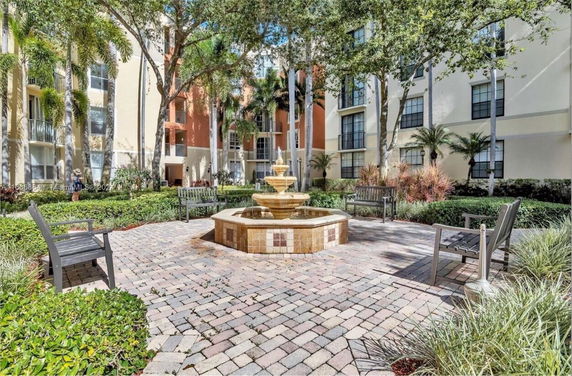 Front view of a multi-story residential building with balconies and landscaped courtyard with a fountain.
