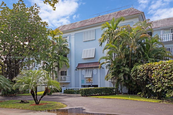 Front view of a multi-story building with balconies and surrounded by palm trees.