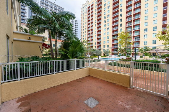 View of a multi-story residential building with balconies, seen from a fenced patio area.