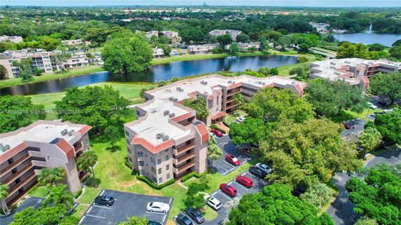 Aerial view of residential buildings surrounded by trees and a river, with parking spaces nearby.