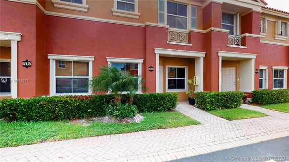 Front view of a multi-story townhouse with a red and beige exterior and small garden.
