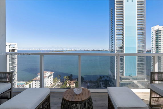 View of the ocean and cityscape from a high-rise balcony with seating area.