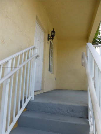 Entrance view of a building with a staircase leading to a white door and a window beside it.