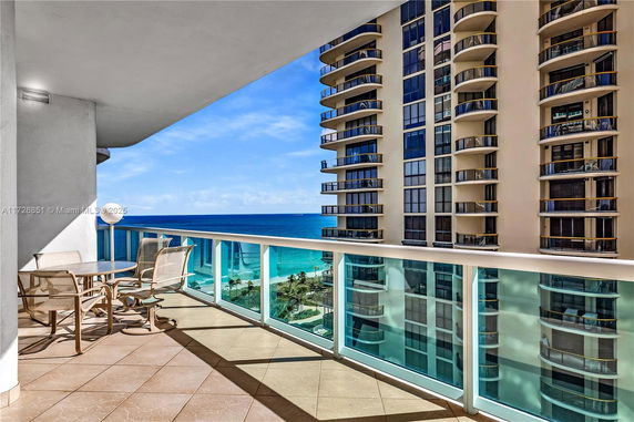 View from a balcony overlooking the ocean and adjacent high-rise buildings.