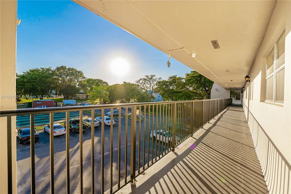 View from a building balcony overlooking a parking area and trees at sunset.
