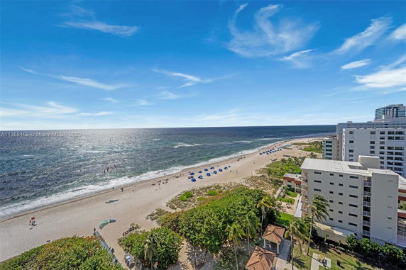 View of a beach with waves, lined with buildings and umbrellas along the shore.