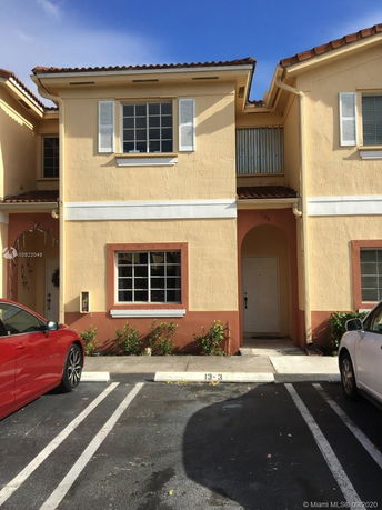 Front view of a two-story house with white shutters and a parking area in front.