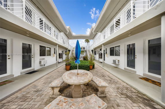 Outdoor view of a two-story building with a central courtyard featuring a stone table and benches under a closed umbrella.