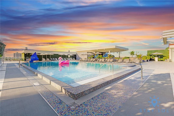 Rooftop area with a large pool and seating, featuring a sunset view.