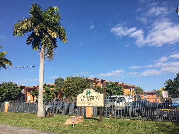 Exterior view of a condominium building with a parking area and palm trees.
