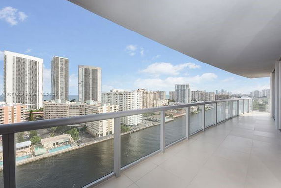 Panoramic view from a building balcony overlooking a river and a city skyline with multiple high-rise buildings.