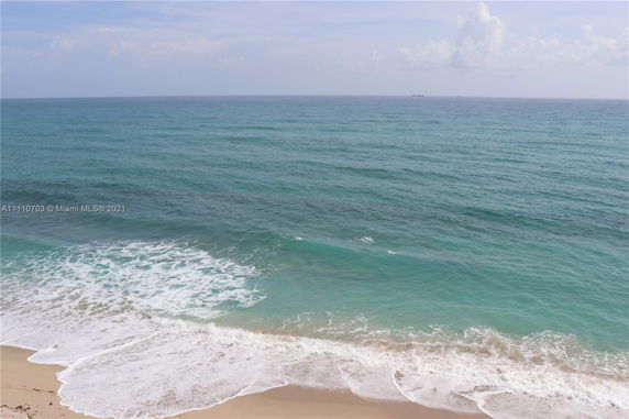 Panoramic view of an ocean with waves reaching the sandy beach.