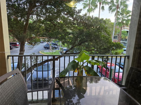View from a balcony overlooking a parking area with trees and several parked cars.