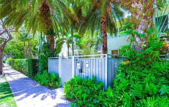 View of building surrounded by palm trees and greenery with a metal fence.