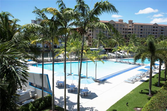 Outdoor swimming pool area with palm trees and lounge chairs.
