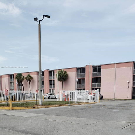 Front view of a multi-story residential building with balconies and a parking area in front.
