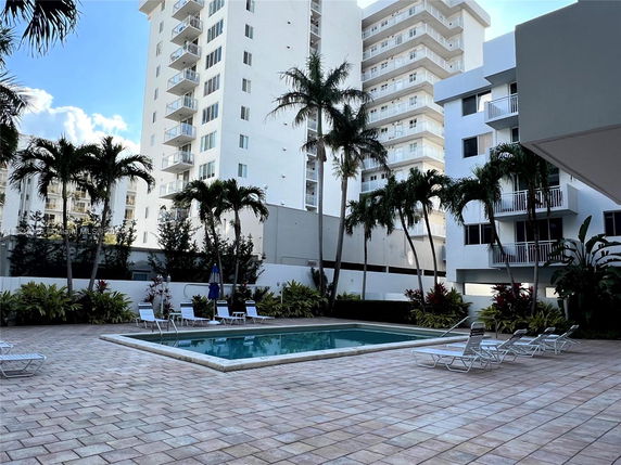 Outdoor swimming pool area with surrounding apartment buildings and palm trees.