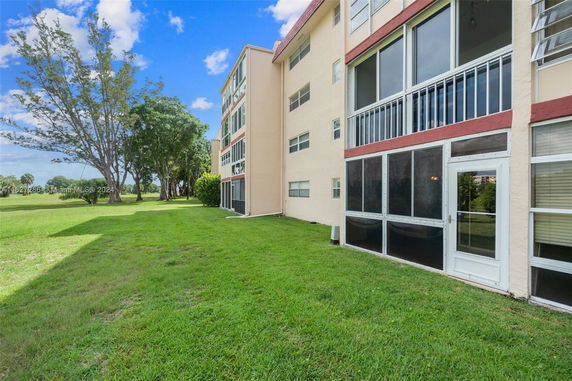 Side view of a multi-story building with enclosed balconies overlooking grassy area.