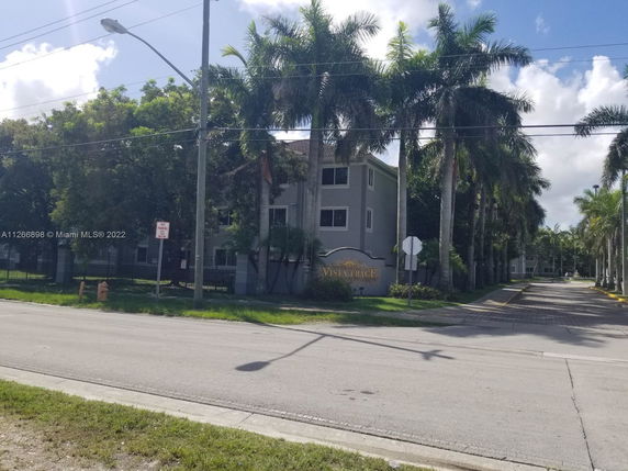 Front view of a multi-story residential building with palm trees lining the entrance.