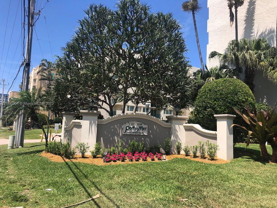 View of a building with a landscaped entrance, featuring a sign and decorative plants.