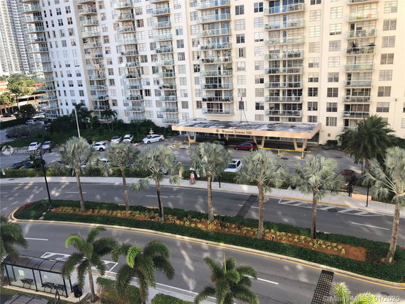 View of a multi-story residential building from a higher level showing palm trees and a driveway.