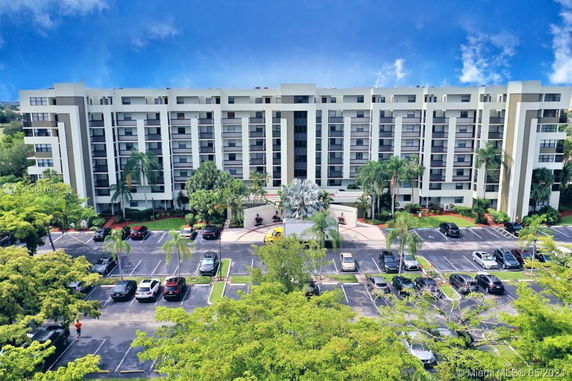 Front view of a multi-story apartment building with balconies and a parking lot in front.