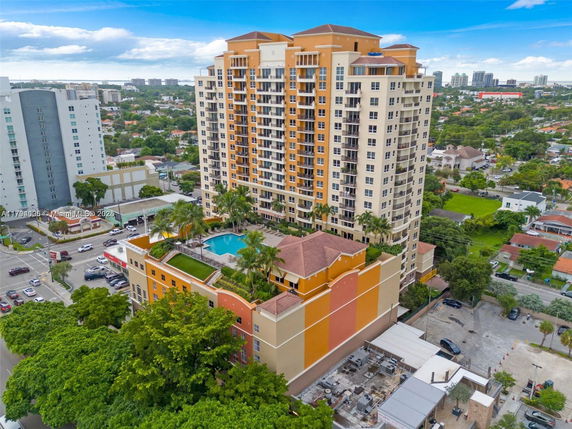 Front view of a tall apartment building with varied colors and balconies, and a rooftop pool area.