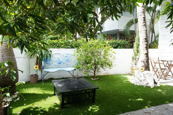 Garden area with a bench, table, and greenery around a building.