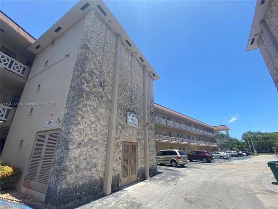 Side view of a multi-story building with stone and stucco exterior, featuring balconies and a parking area.