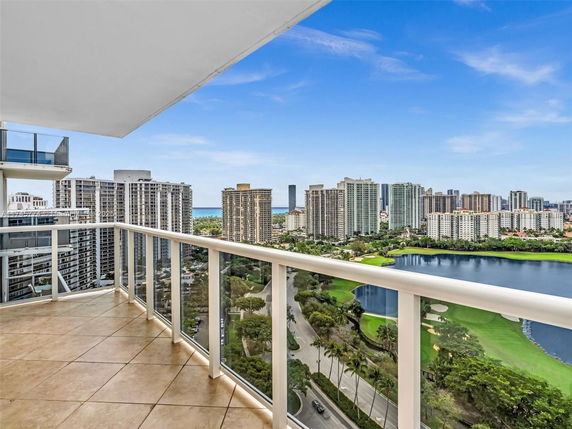 Panoramic view from a balcony overlooking city buildings and a golf course with water features.