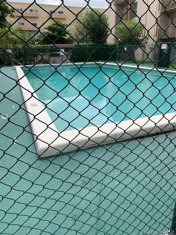 Outdoor swimming pool surrounded by a fence, with a building in the background.