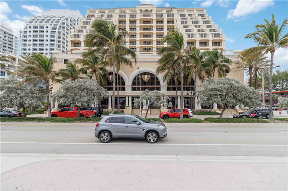 Front view of a multi-story building with large windows and palm trees in front.