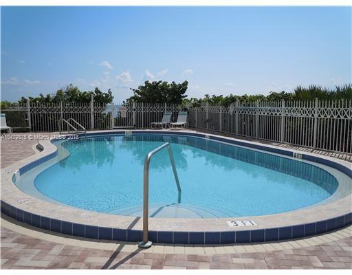 Outdoor swimming pool with metal railing surrounded by a fence and greenery.
