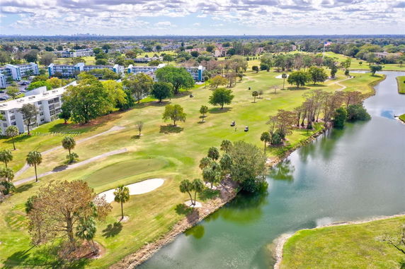 Aerial view of a golf course with nearby residential buildings and a water body.