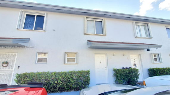 Front view of a two-story apartment building with white exterior walls and small shrubs in front.