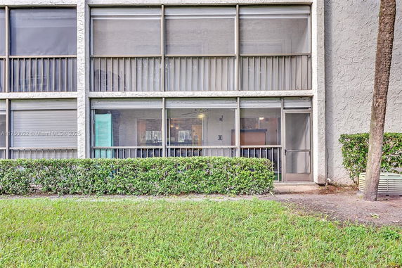 Front view of a building with large screened windows and a hedge.