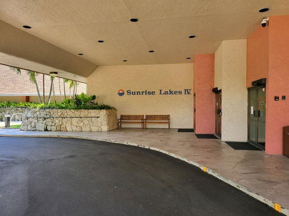 Entrance area of a building marked Sunrise Lakes IV with benches and a covered driveway.