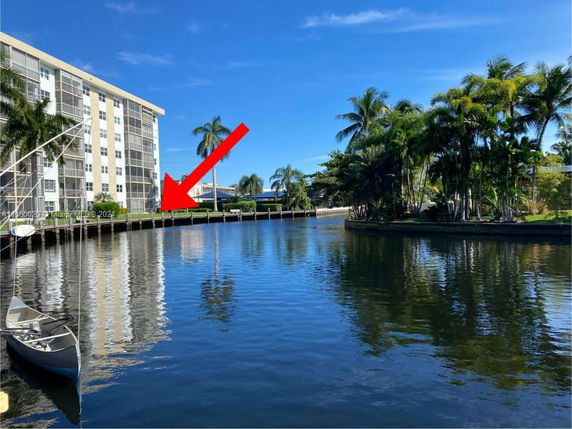 View of a canal with a multi-story building on the left, surrounded by palm trees.