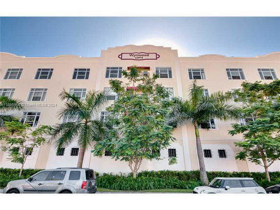 Front view of a multi-story building with multiple windows and palm trees in front.