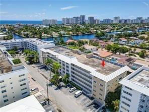 Aerial view of a multi-story apartment building with a flat rooftop, surrounded by other buildings and waterways.