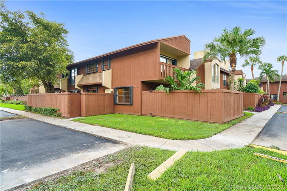 Front view of a two-story townhouse with wooden siding and fenced yard.