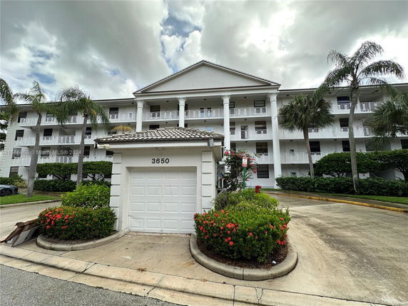 Front view of a multi-story residential building with white railings and columns, featuring a small building with the number 3650 in front.