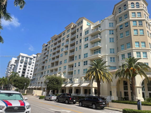 Front view of a multi-story apartment building with balconies and palm trees in front.