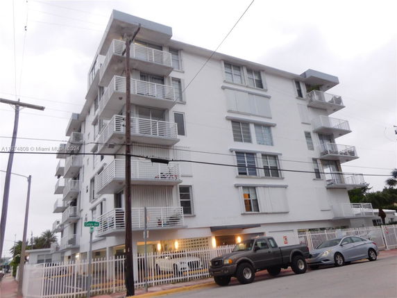 Front view of a multi-story apartment building with balconies and a gated parking area.