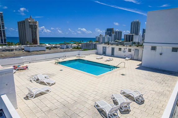 Rooftop with swimming pool and lounge chairs, overlooking city and ocean.