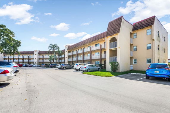 Front view of a three-story residential building with balconies and a parking area.