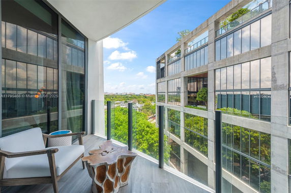 View from a balcony overlooking modern buildings with large glass windows and a lush green area.