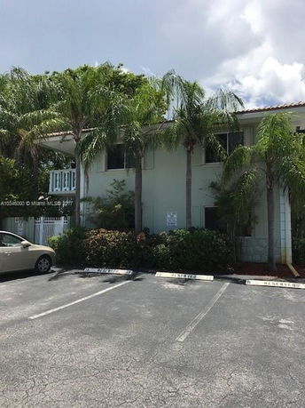 Front view of a two-story residential building with palm trees and a parking area.