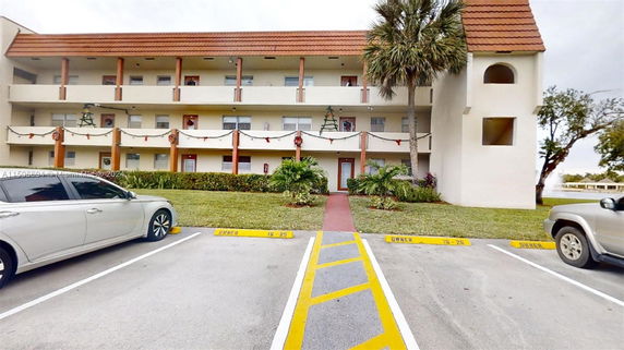 Front view of a multi-story building with balconies and parking area in front.