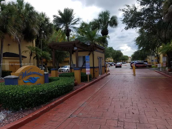 Driveway and entrance area of a residential complex with palm trees and parked cars.